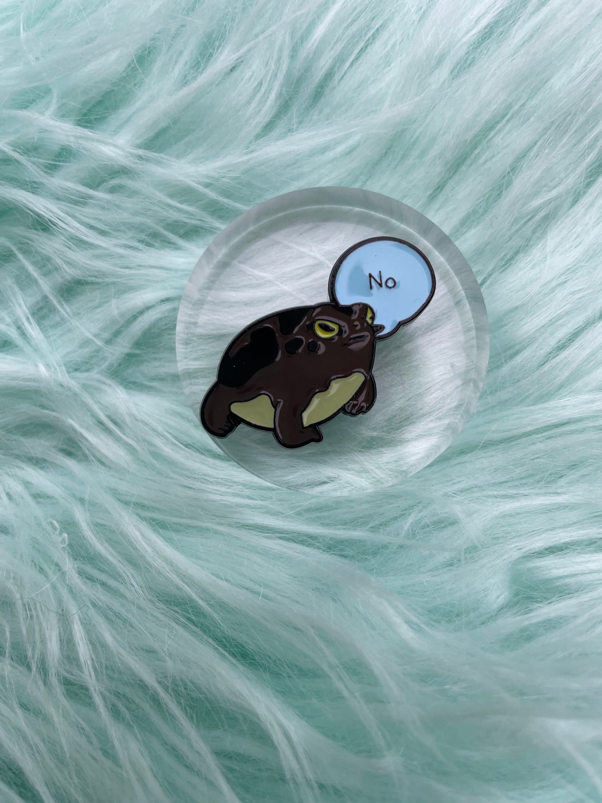 Frog saying no, enamel pin on blue fur and round plastic stand