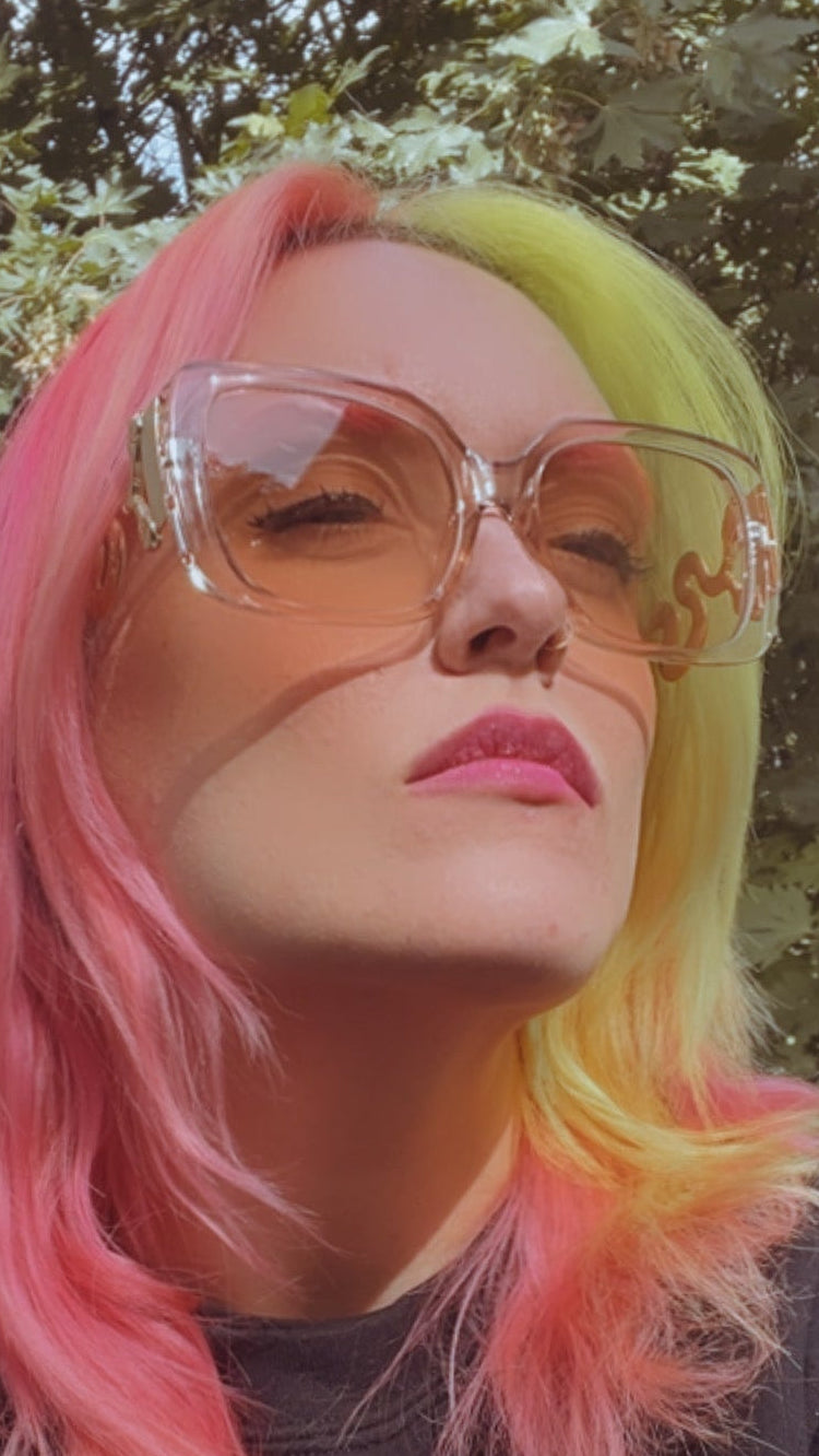 A person wearing sunglasses with a colorful hair and a black sweatshirt with text on it.